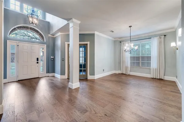 an empty room with wooden floor chandelier and windows