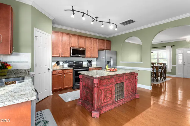 a large kitchen with stainless steel appliances granite countertop a stove a sink dishwasher a microwave oven and a dining table with wooden floor