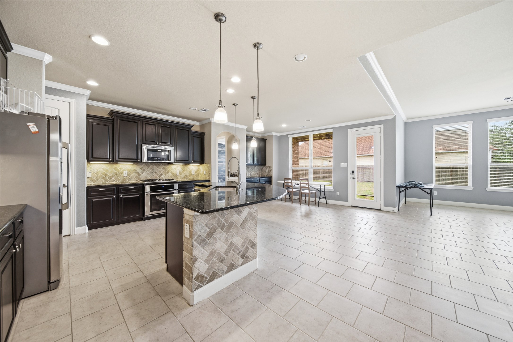 5303 Mesquite Willow Lane Rosharon, TX 77583 - Photo 12 of 32 This kitchen features modern stainless steel appliances, dark cabinetry, and a large island with pendant lighting. It opens to a bright, tiled dining area with large windows and a door leading to the backyard, perfect for entertaining.