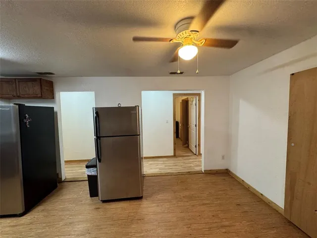 a view of a refrigerator in kitchen and an empty room with wooden floor