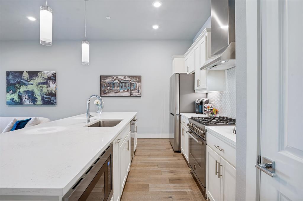 15875 Spectrum Drive, Unit 1101 Addison, TX 75001 - Photo 13 of 37 Modern kitchen featuring white cabinetry, stainless steel appliances, a large island with an undermount sink, and wood-finish flooring