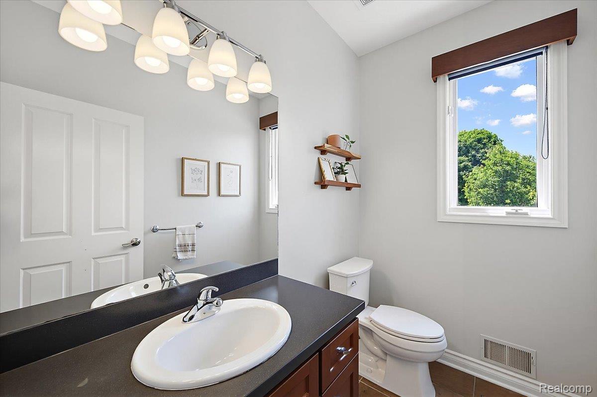 1422 Galena Rochester, MI 48306 - Photo 24 of 73 Bathroom featuring a single-sink vanity with a dark countertop and wood-finish cabinetry, a large wall-mounted mirror, a multi-bulb light fixture, a white toilet, and a window with exterior tree views