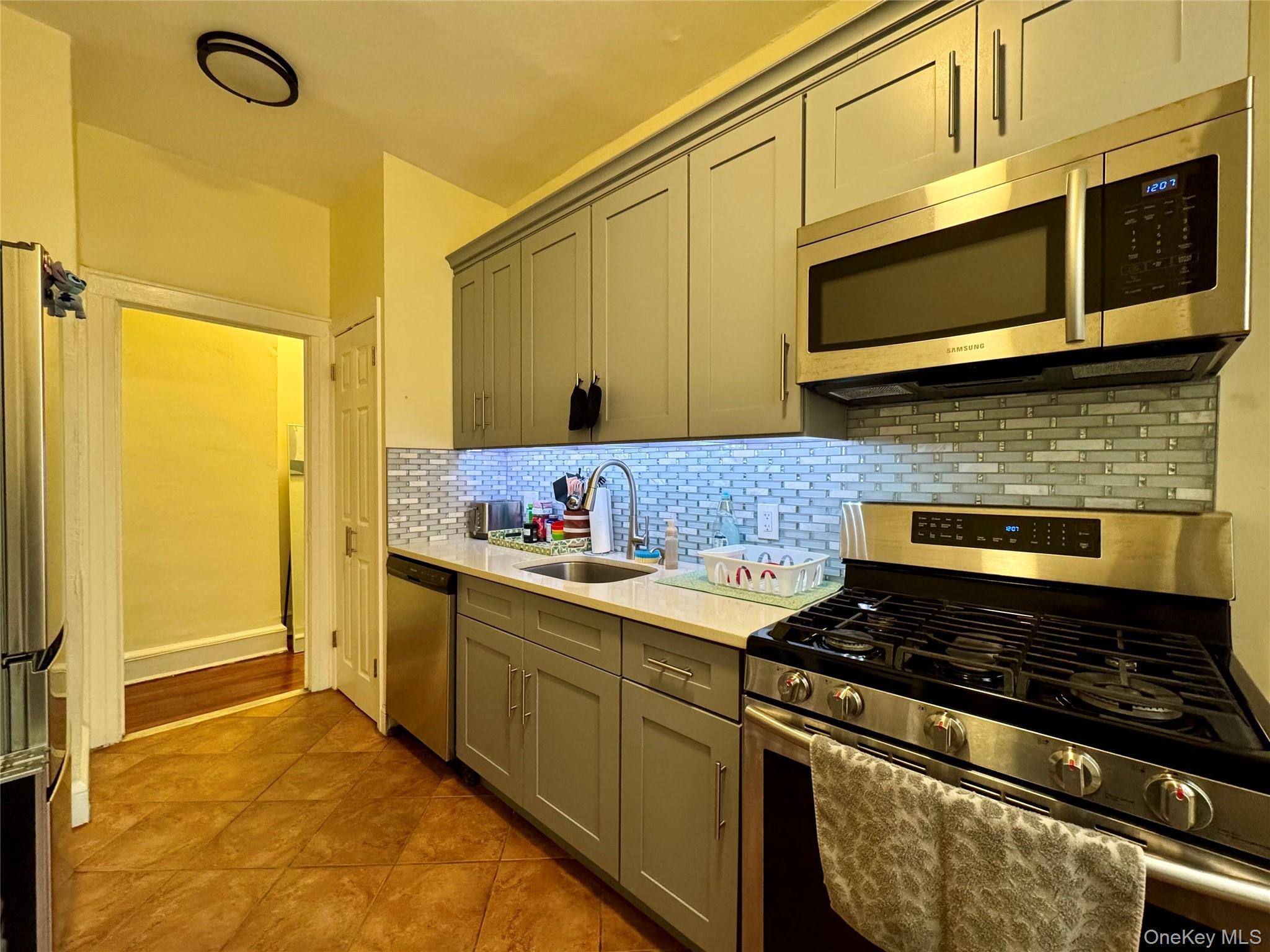 83-64 Talbot Street, Unit 3A Queens, NY 11415 - Photo 1 of 19 Kitchen featuring stainless steel appliances, gray cabinets, backsplash, light stone countertops, and light tile patterned floors