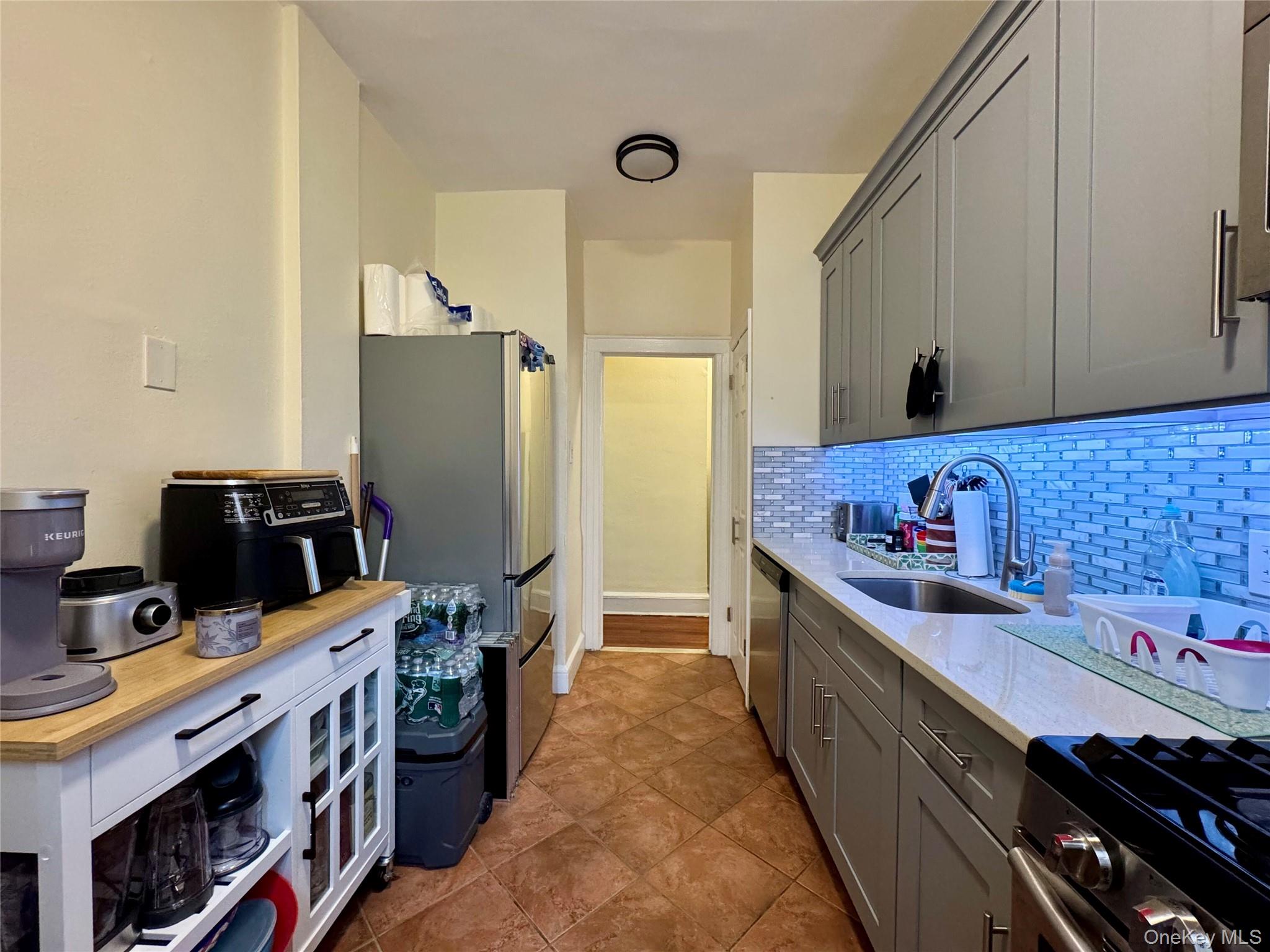 83-64 Talbot Street, Unit 3A Queens, NY 11415 - Photo 3 of 19 Kitchen with gray cabinetry, stainless steel appliances, light stone countertops, and decorative backsplash