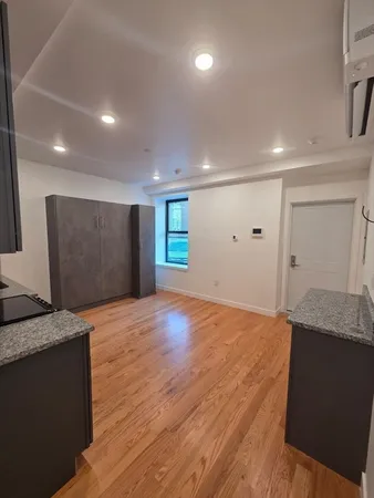 a view of an empty room with kitchen and window