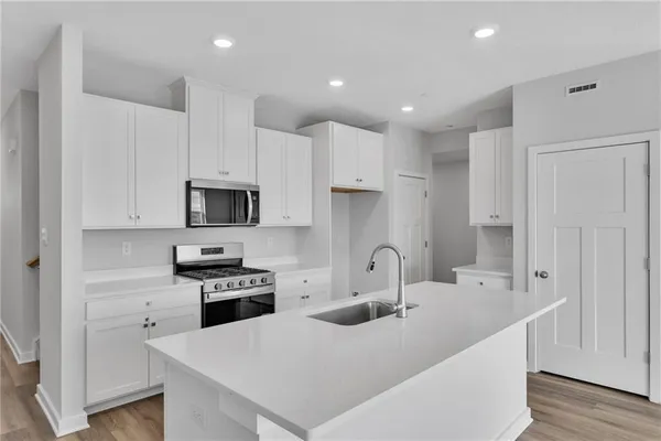 a kitchen with stainless steel appliances a sink a stove a microwave a refrigerator a white cabinets and wooden floor