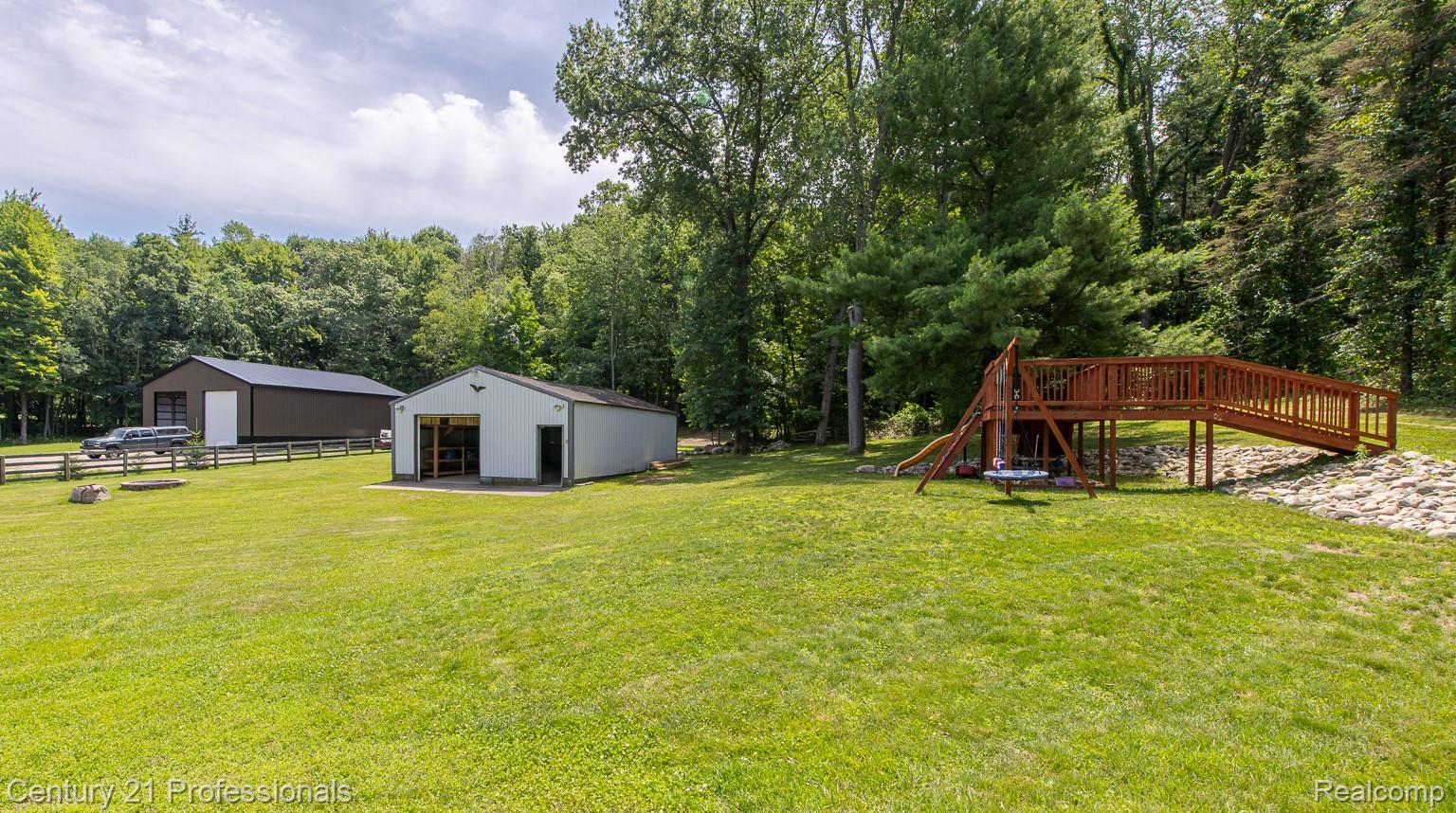 1790 Kent Road Ortonville, MI 48462 - Photo 46 of 64 Expansive green lawn with a large brown metal-sided building, a white metal-sided outbuilding, and a multi-level wooden play structure