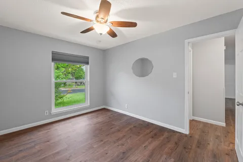 an empty room with wooden floor fan and windows