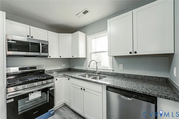 a kitchen with granite countertop a sink a stove a microwave and cabinets