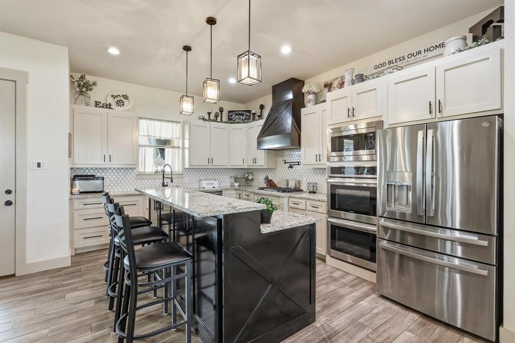 6020 Honeysuckle Road Midlothian, TX 76065 - Photo 13 of 39 Gourmet kitchen featuring a large island with seating, stainless steel appliances, white cabinetry, granite countertops, and a decorative range hood