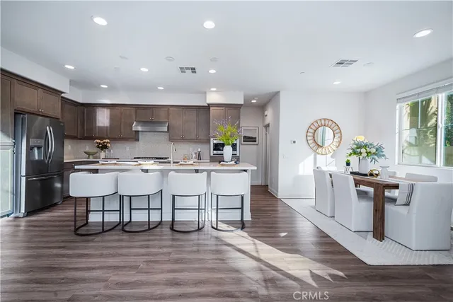 a kitchen with stainless steel appliances granite countertop a refrigerator a sink dishwasher a dining table and chairs with wooden floor