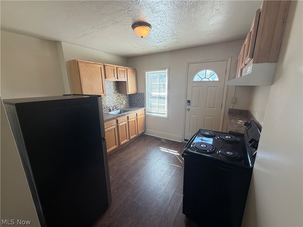 15416 Waterloo Road Cleveland, OH 44110 - Photo 7 of 18 Kitchen featuring wood-finish flooring, light wood cabinetry, a mosaic tile backsplash, and a white exterior door with an arched window