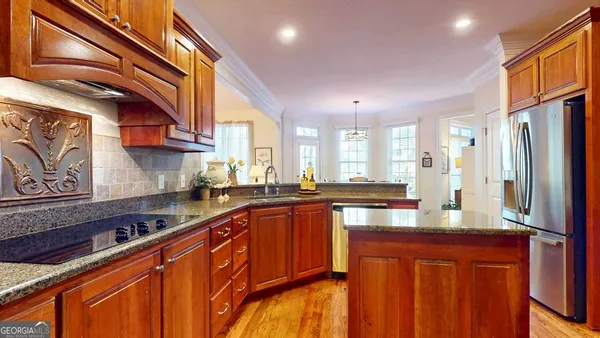 a large kitchen with stainless steel appliances granite countertop a refrigerator a sink dishwasher a stove and a dining table with wooden cabinet