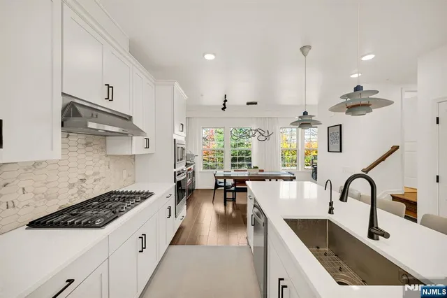 a kitchen with granite countertop a stove a sink a refrigerator and white cabinets with wooden floor