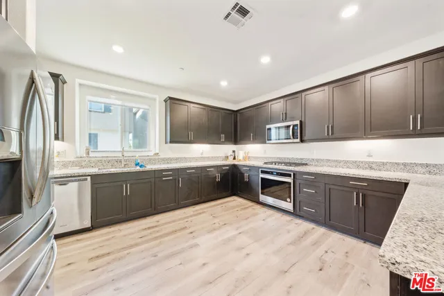 a large kitchen with stainless steel appliances granite countertop a sink stove refrigerator granite counter tops wooden cabinets and wooden floor