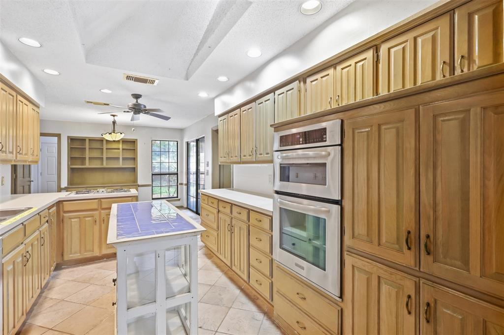 37 Timbergreen Circle Denton, TX 76205 - Photo 18 of 31 Spacious kitchen featuring extensive wood cabinetry, tile flooring, built-in double ovens, white countertops, and a central island with a tiled surface
