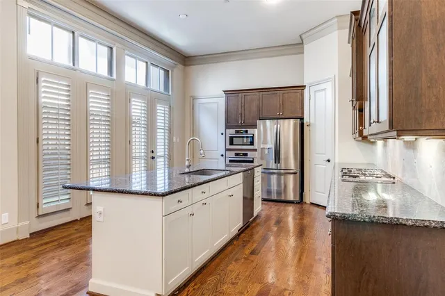 a kitchen with stainless steel appliances granite countertop a refrigerator a sink dishwasher a stove and white countertops with wooden floor