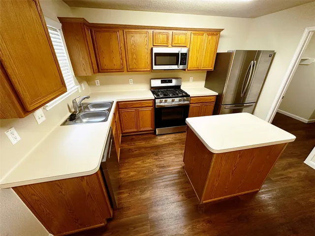 a kitchen with stainless steel appliances a stove a sink a microwave a refrigerator a sink a refrigerator white cabinets and wooden floor