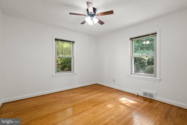 an empty room with wooden floor chandelier fan and windows