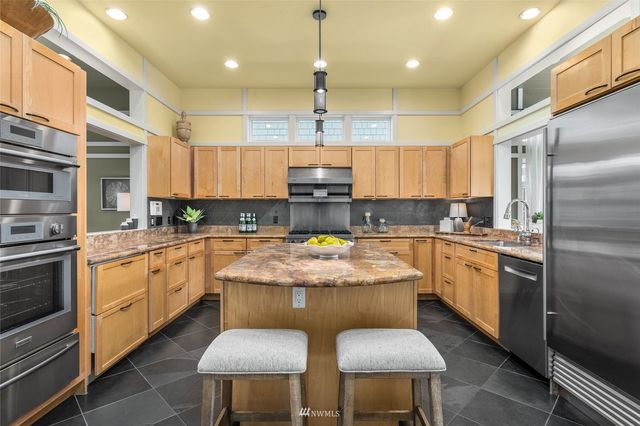 a large kitchen with stainless steel appliances granite countertop a stove a sink dishwasher and a refrigerator with wooden cabinets