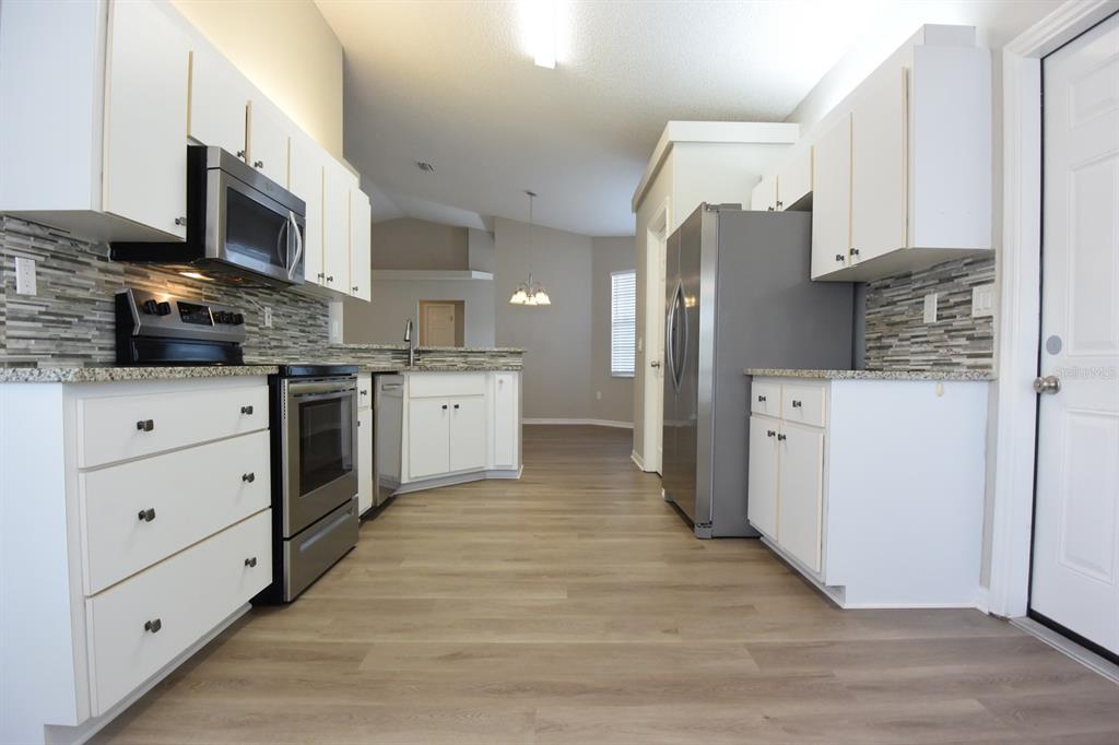 2339 Renton Lane Spring Hill, FL 34609 - Photo 13 of 35 a kitchen with stainless steel appliances kitchen island granite countertop a stove top oven a sink dishwasher and a refrigerator with wooden floor
