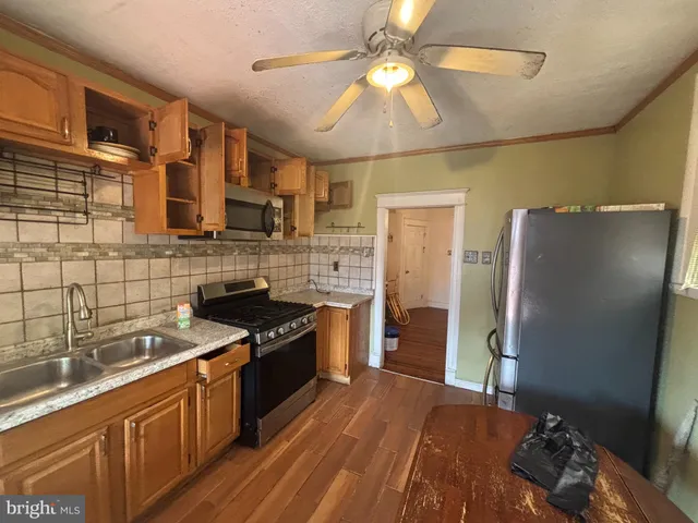 a kitchen with stainless steel appliances granite countertop a refrigerator a sink dishwasher a stove and a dining table with wooden floor