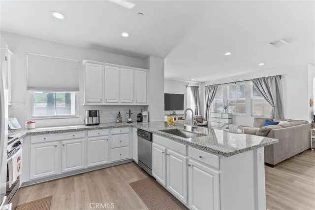 a kitchen with stainless steel appliances granite countertop a sink dishwasher a stove and white cabinets with wooden floor