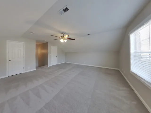 an empty room with chandelier fan and windows
