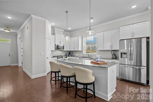 a kitchen with stainless steel appliances granite countertop a refrigerator a sink dishwasher a stove and white cabinets with wooden floor