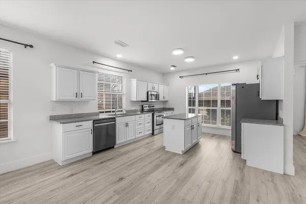 a large kitchen with kitchen island wooden floors white cabinets and stainless steel appliances