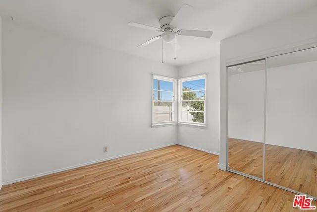 an empty room with wooden floor chandelier fan and windows