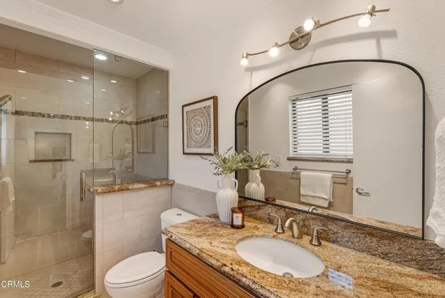 a bathroom with a granite countertop sink a toilet a mirror and shower