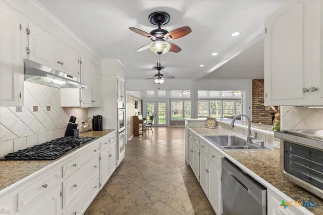 a large kitchen with stainless steel appliances kitchen island granite countertop a stove a sink dishwasher and white cabinets with wooden floor
