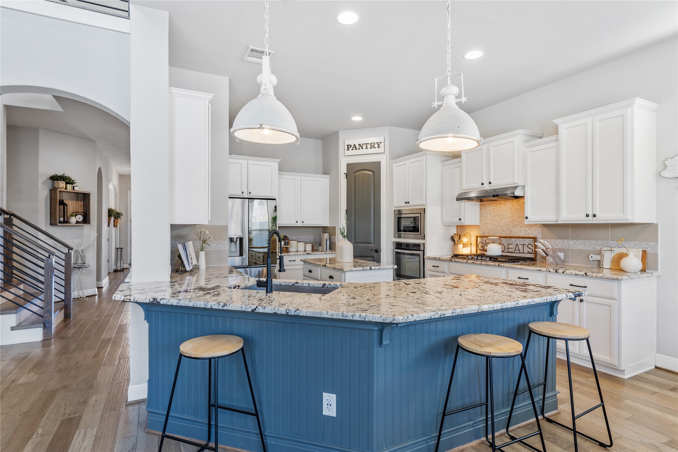 20524 Fairleaf Street Pflugerville, TX 78660 - Photo 6 of 35 Kitchen featuring a breakfast bar area, light wood-type flooring, a peninsula, arched walkways, and white cabinets