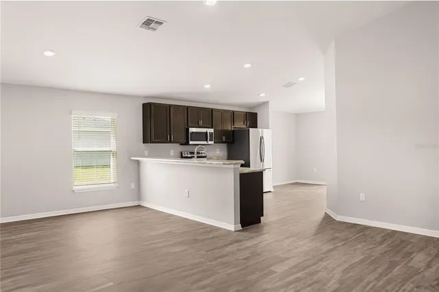 a view of kitchen with stainless steel appliances kitchen island wooden floors and white walls
