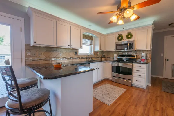 a kitchen with granite countertop a stove top oven a sink dishwasher and white cabinets with wooden floor