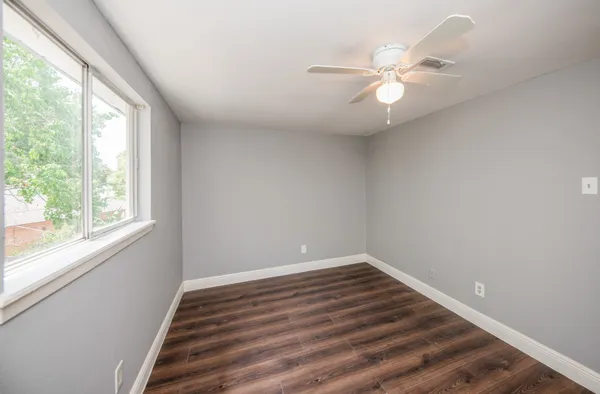 an empty room with wooden floor fan and windows