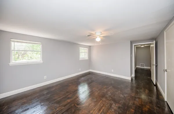 an empty room with wooden floor chandelier fan and windows