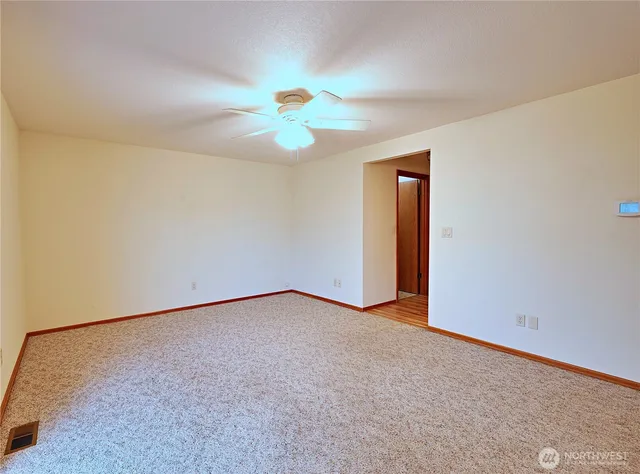 an empty room with a chandelier fan and windows