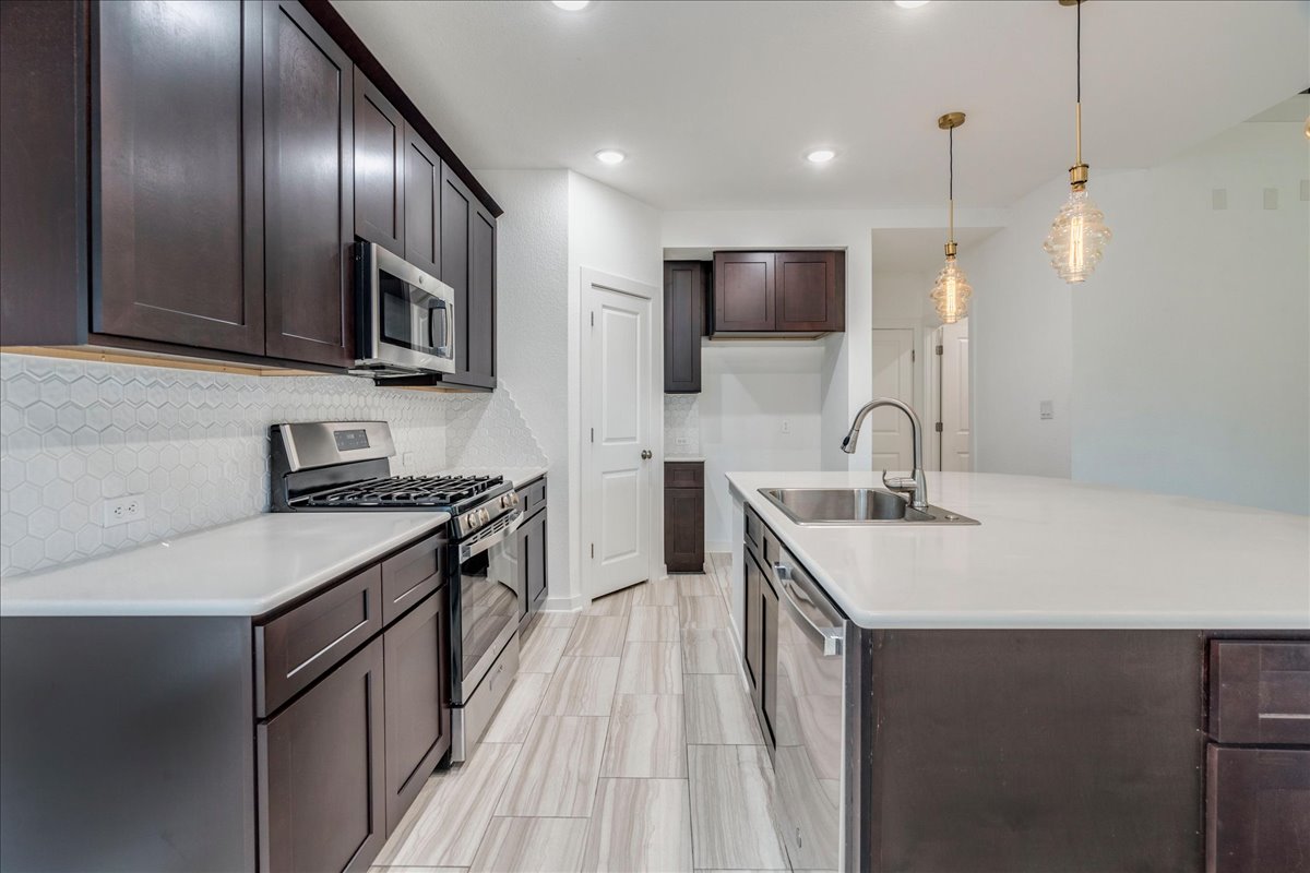 8008 Prairie Rye Drive Lago Vista, TX 78645 - Photo 22 of 40 Modern kitchen featuring dark wood cabinetry, stainless steel appliances, a white solid surface countertop, and a white geometric tile backsplash