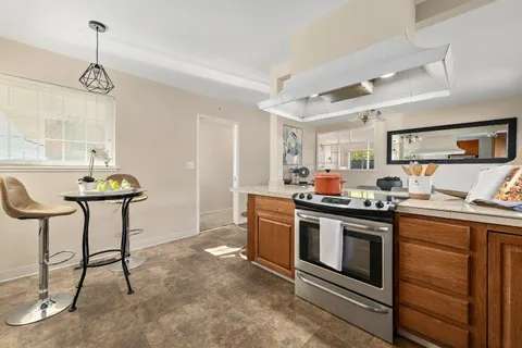 a kitchen with stainless steel appliances a stove a sink dishwasher a dining table and chairs with wooden floor