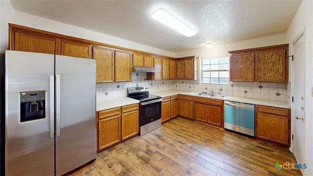 a kitchen with stainless steel appliances granite countertop a refrigerator a sink dishwasher a oven with wooden cabinets and a window