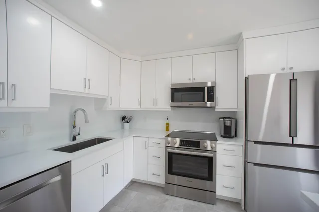 a kitchen with stainless steel appliances granite countertop a refrigerator stove a sink and white cabinets