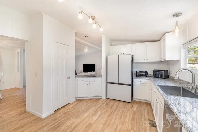 a kitchen with granite countertop a refrigerator oven a sink dishwasher and white cabinets with wooden floor