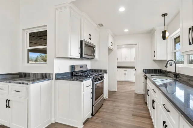 a kitchen with stainless steel appliances granite countertop a stove top oven a sink a refrigerator white cabinets and wooden floor