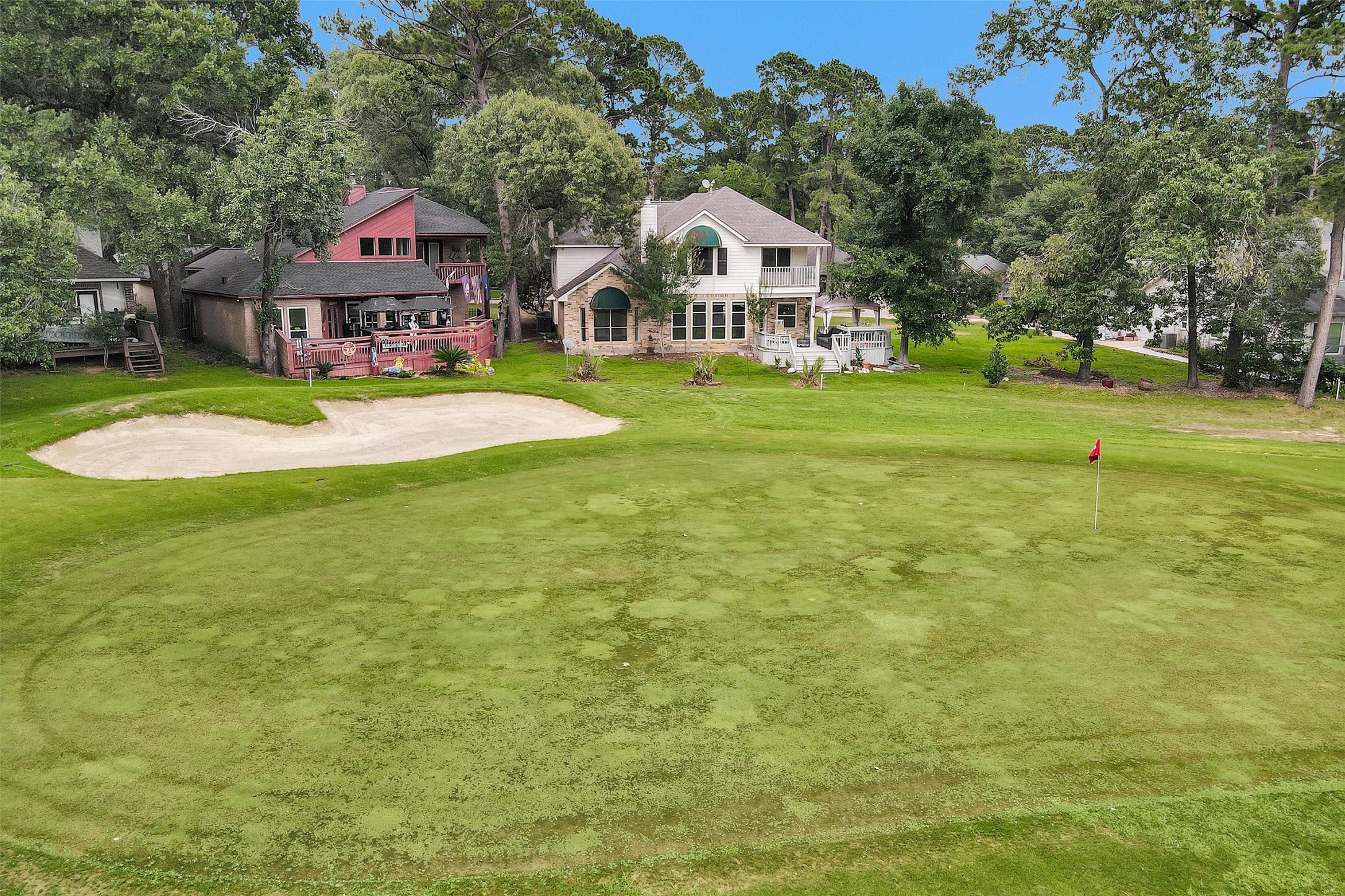 23 Alba Road Montgomery, TX 77356 - Photo 35 of 37 This photo showcases a row of charming homes with decks overlooking a lush golf course, complete with a sand trap and a putting green. Surrounded by mature trees, the setting offers a serene and picturesque view, ideal for golf enthusiasts and nature lovers alike.