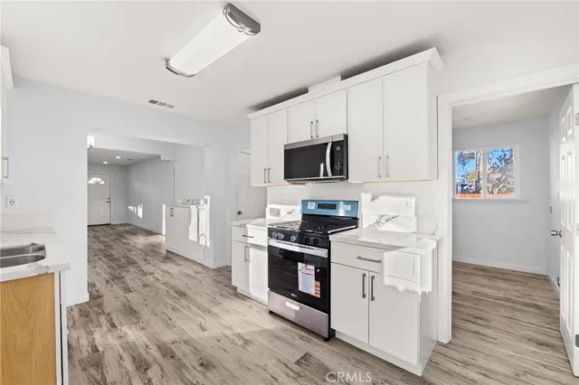 a kitchen with stainless steel appliances a stove top oven a sink a refrigerator white cabinets and wooden floor