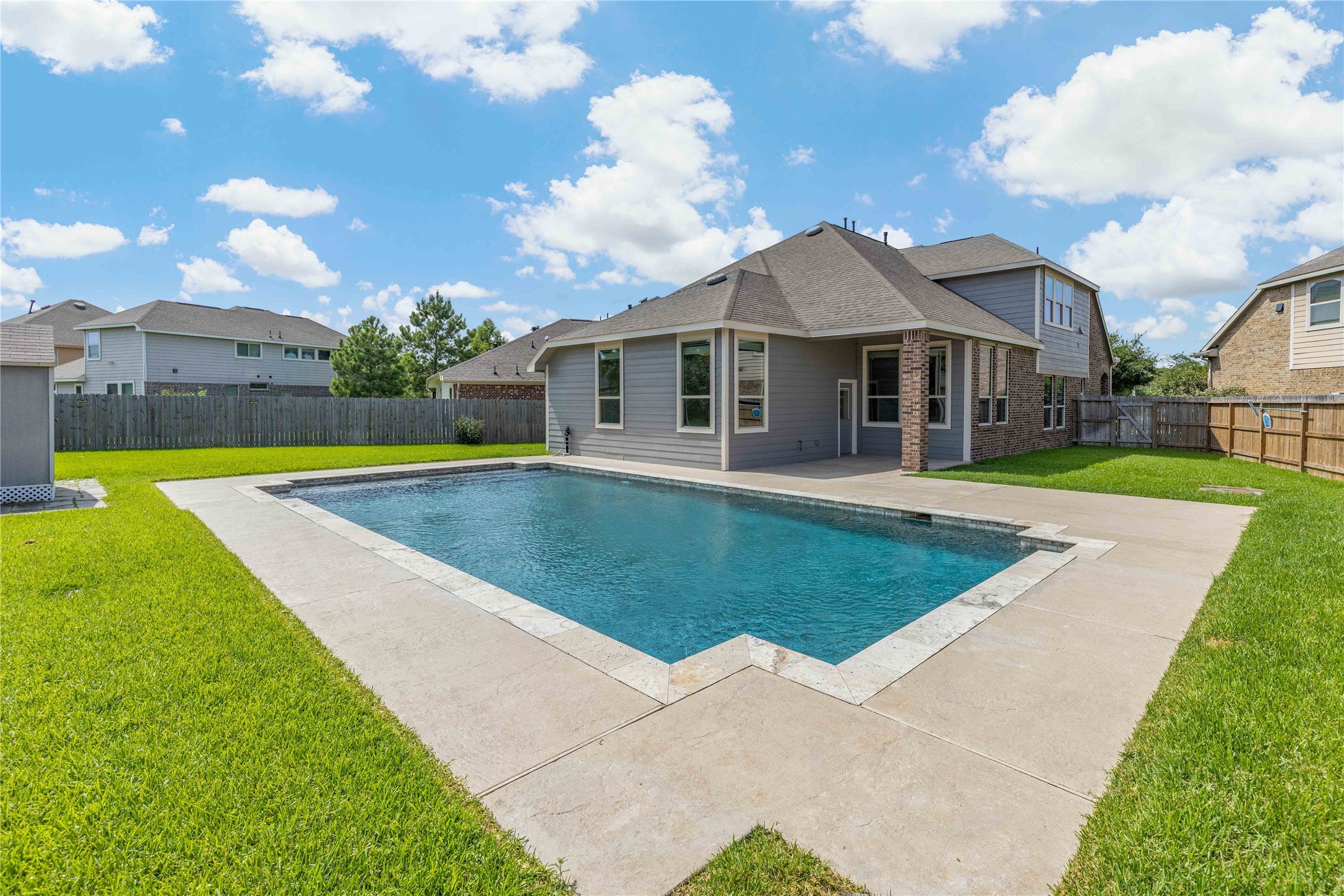 17206 Upper Ridge Lane Humble, TX 77346 - Photo 41 of 50 A spacious backyard with a modern rectangular pool, bordered by a well-maintained lawn and a patio area connected to a two-story house. The surrounding fence ensures privacy, making it ideal for relaxation and entertaining.