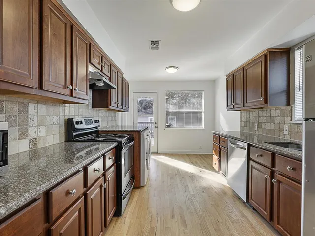 a kitchen with stainless steel appliances granite countertop wooden cabinets a sink a stove a washer and dryer