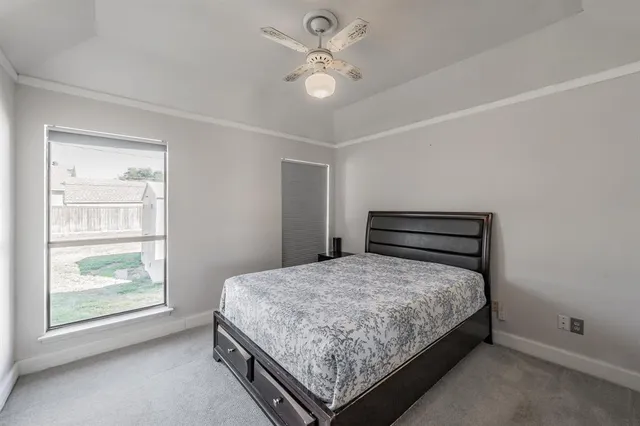 a bedroom with a bed and a large window with ceiling fan